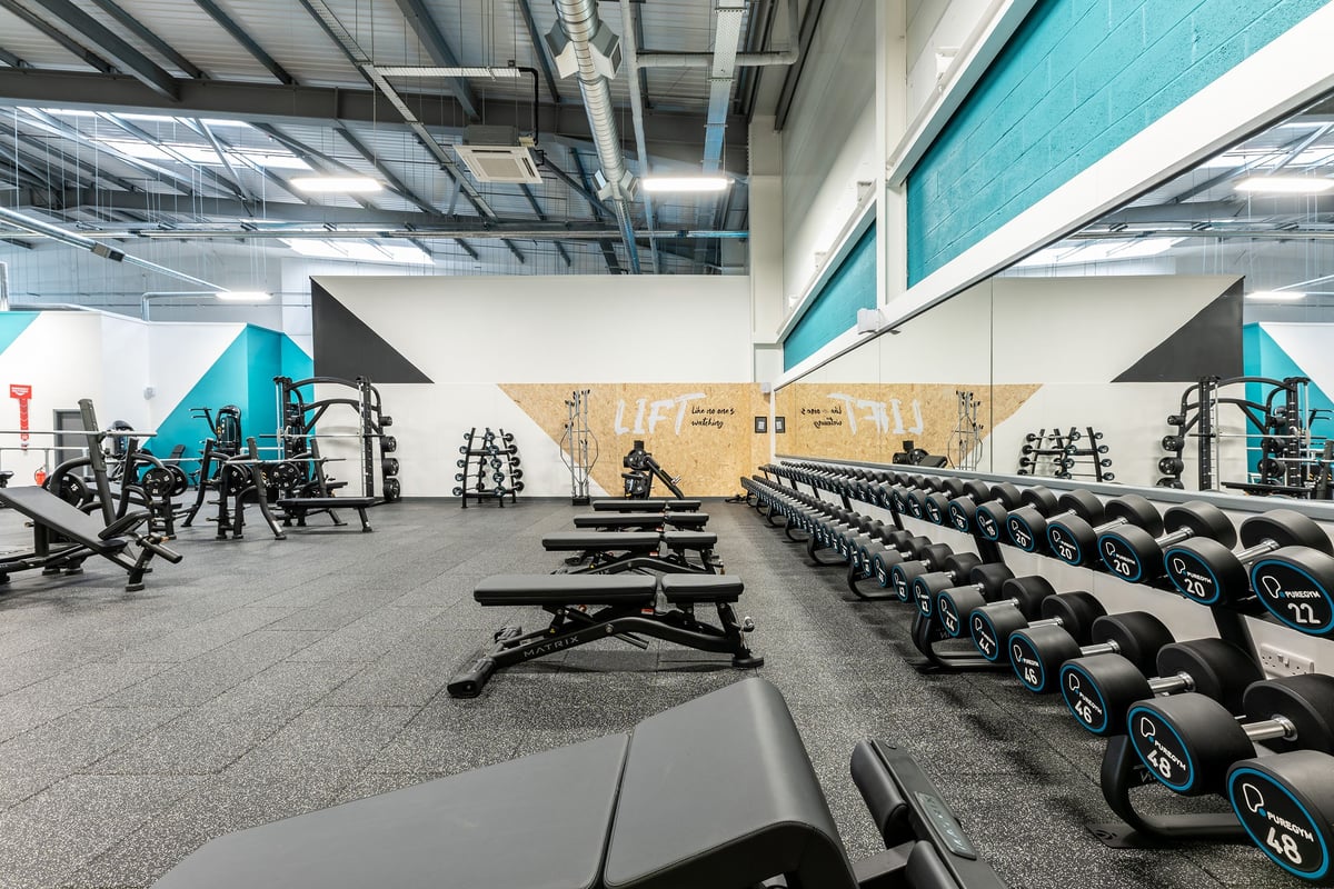 PureGym Kirkby: Weightlifting area with squat racks, benches, dumbbells, weight plates, and rubberized floors.