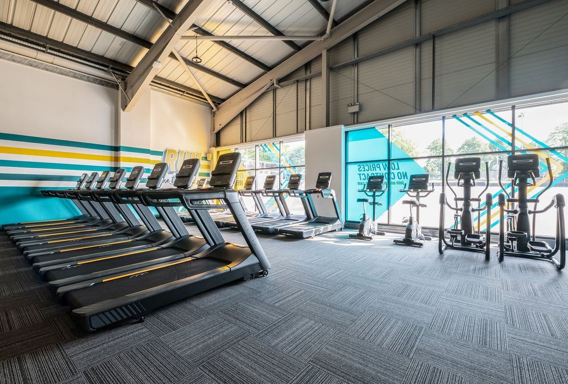 PureGym Leeds Bramley: Rows of treadmills, ellipticals, and weight machines in a bright gym interior.