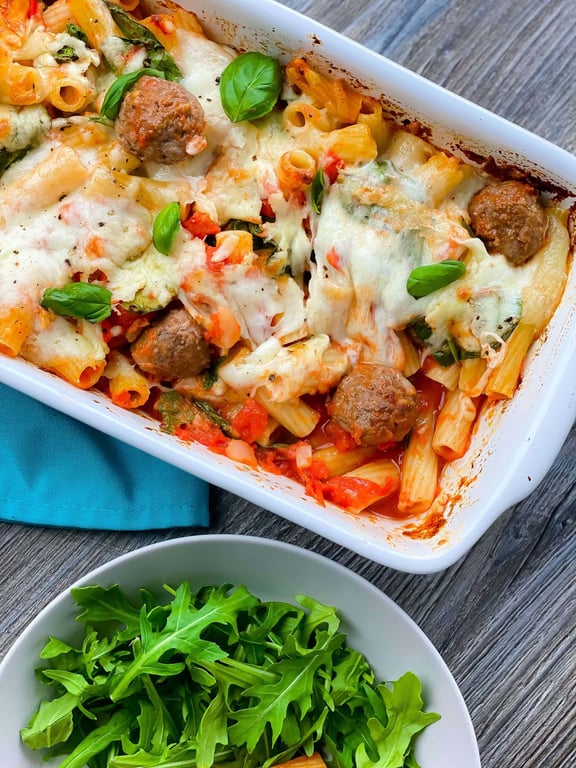 Baked pasta with meatballs, melted cheese, tomato sauce, and fresh basil leaves