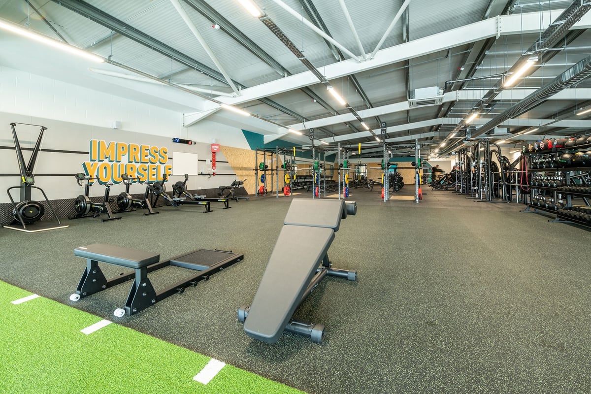 PureGym London Colney: Gym with weight racks, benches, rubberized flooring, motivational mural "Express Yourself" on wall.