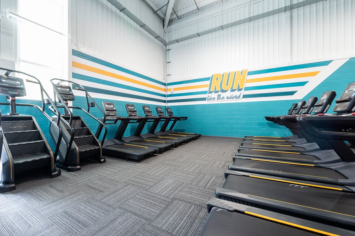 PureGym Winchester: Rows of treadmills with motivational wall mural encouraging exercise.