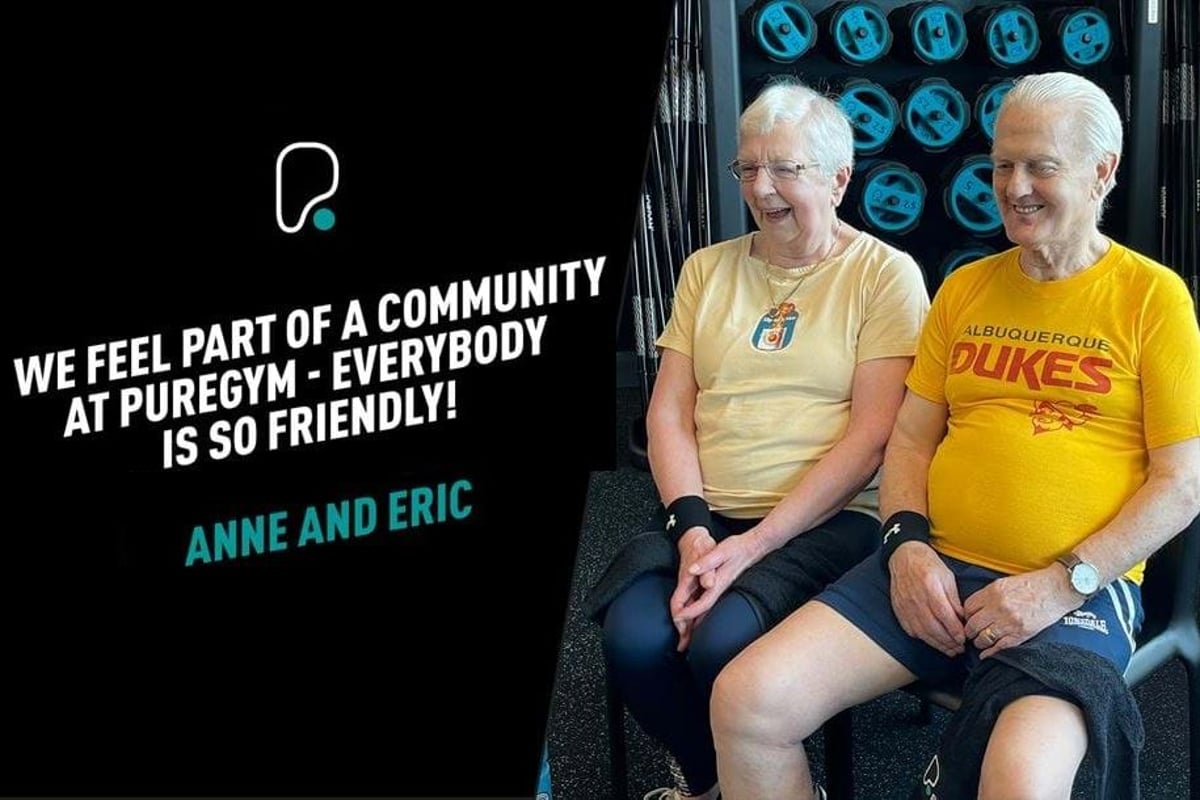 Two elderly people sitting and smiling in a gym with weights in the background