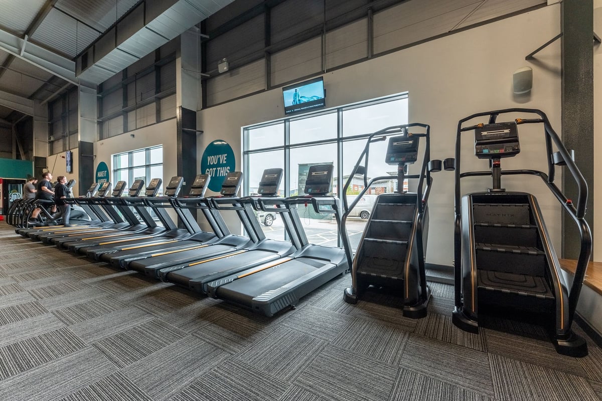 PureGym Widnes: Rows of treadmills, stair climbers, and other cardio equipment in a modern gym setting.