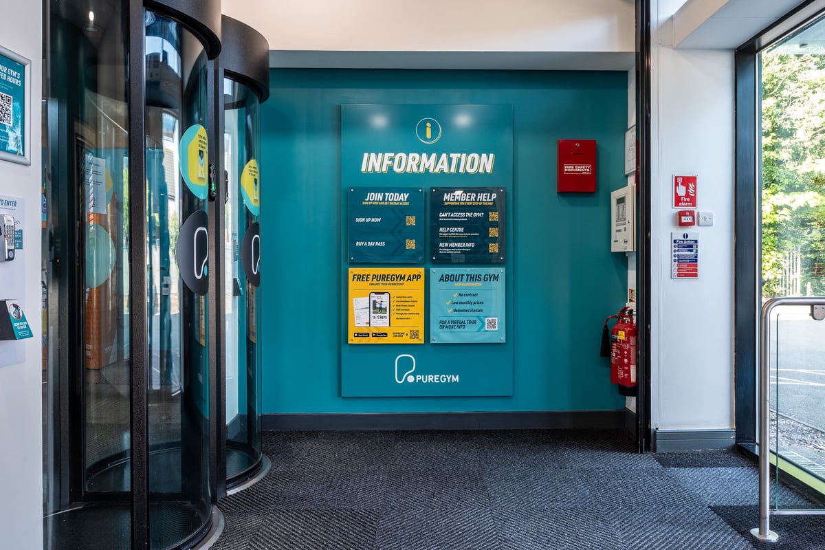 PureGym Sutton Coldfield: Entrance area with information desk, signage about joining and fire extinguisher.