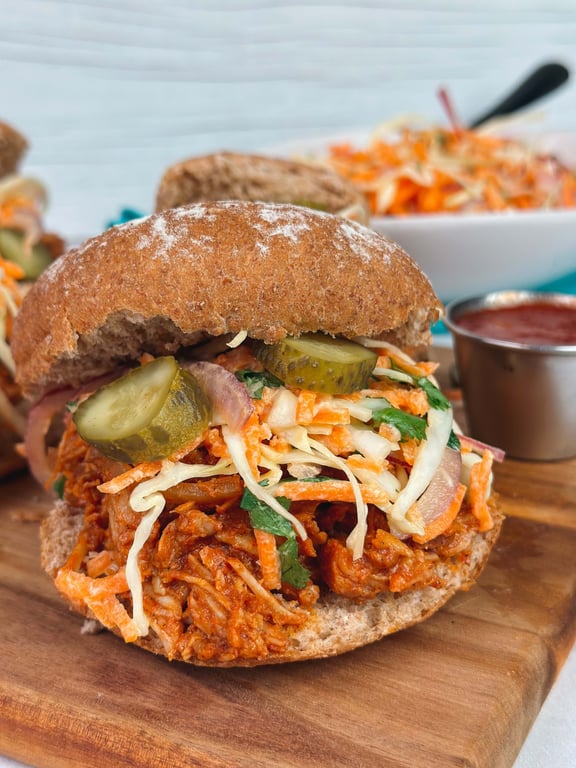 Pulled chicken sandwich with pickles and coleslaw on whole wheat bun on wooden board
