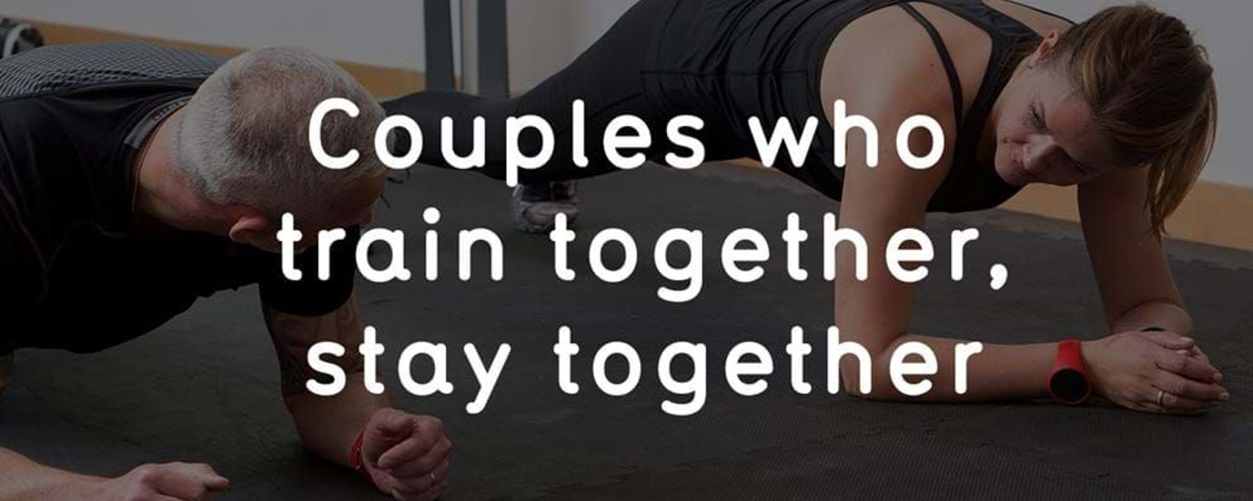 Couple doing plank exercise side by side on a gym mat indoors