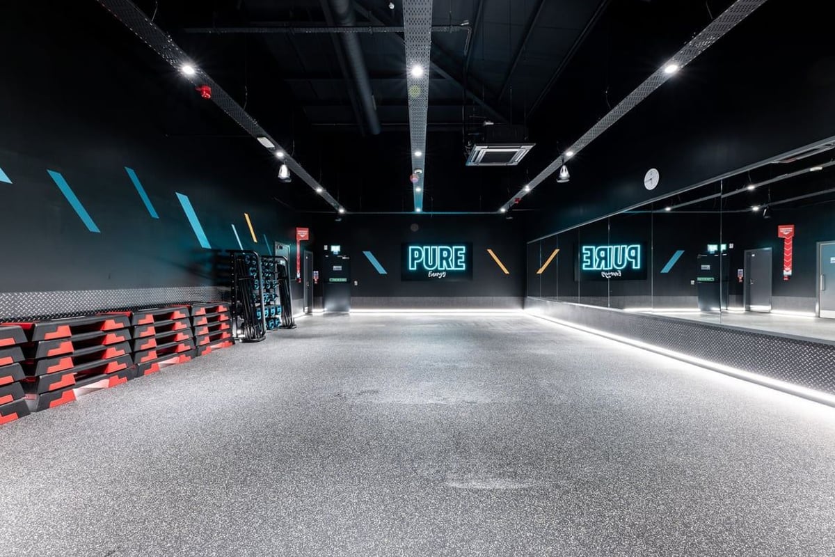 PureGym Dumfries: Rows of red weight racks, wall mirrors, blue neon signage, and rubberized floors.
