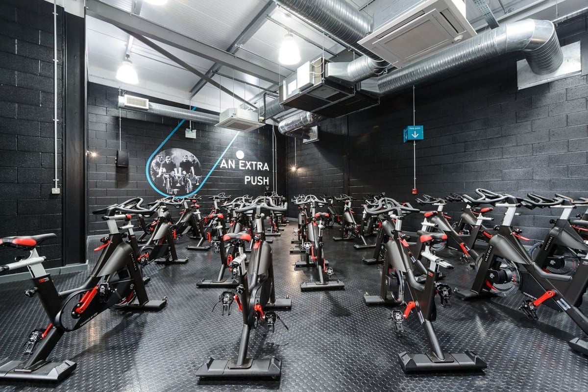 PureGym Leeds Regent Street: Rows of stationary exercise bikes in a dimly lit studio with exposed ducts and brick walls.