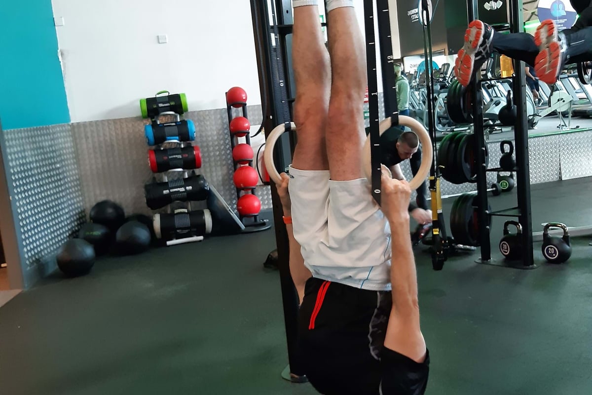 Man hanging upside down on gymnastic rings in a gym with exercise equipment around