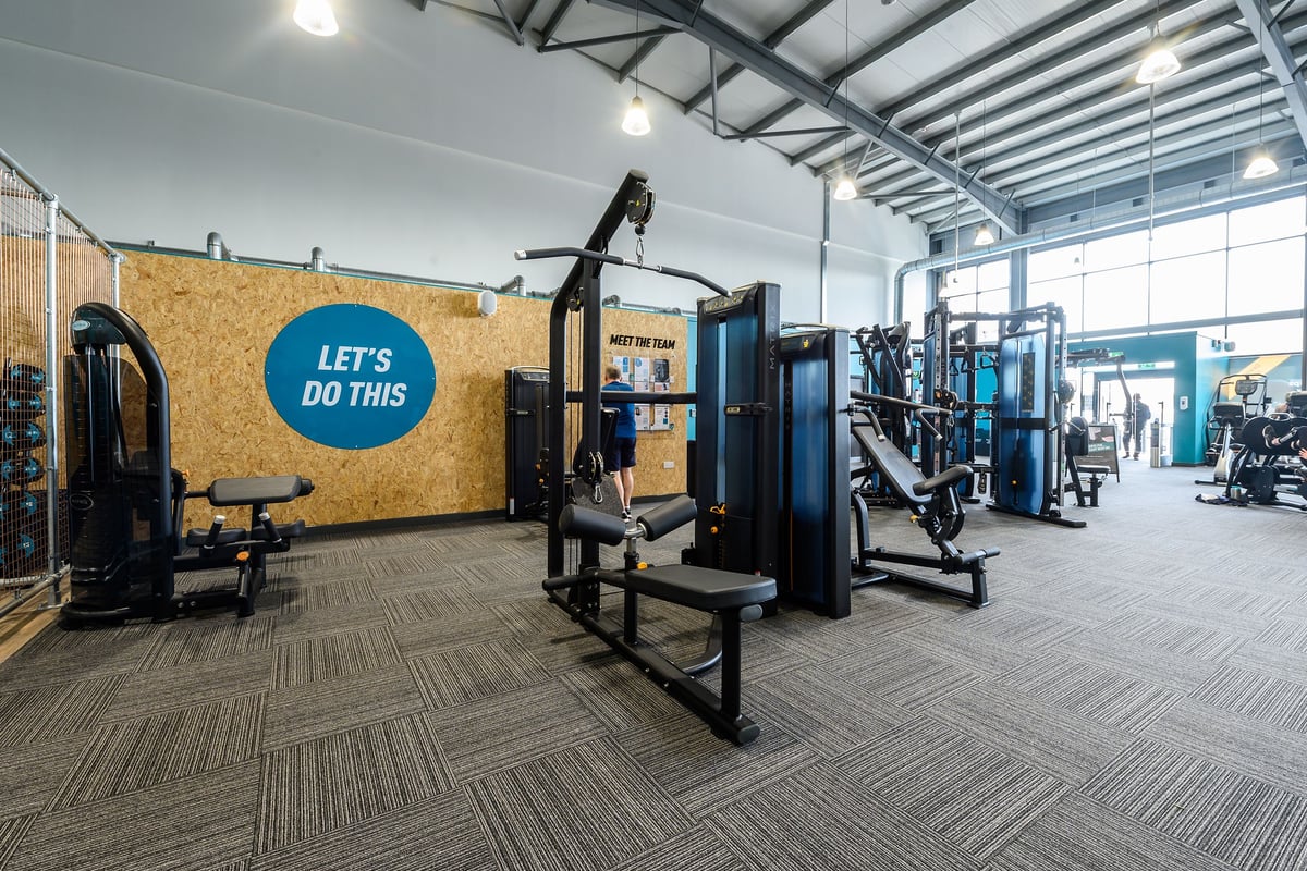 PureGym Maldon Blackwater Retail Park: Workout area with weight machines, benches, mirrored wall, and motivational signage.