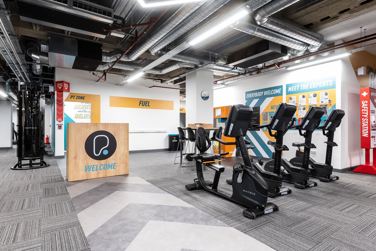 PureGym London Monument: Rows of stationary exercise bikes, signage boards, and an open gym area with industrial ceiling.