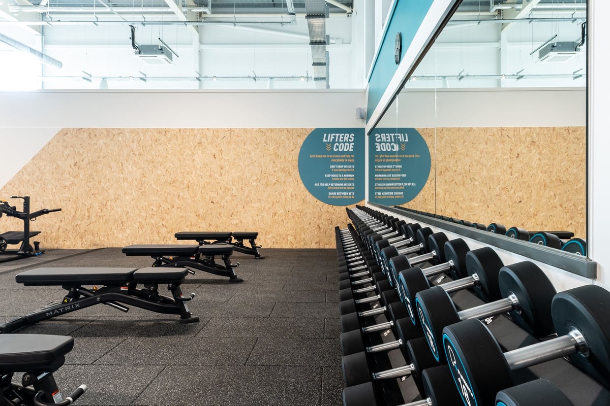 PureGym St Ives Cambridgeshire: Rows of benches, free weights, squat racks, and rubberized flooring in a gym studio.