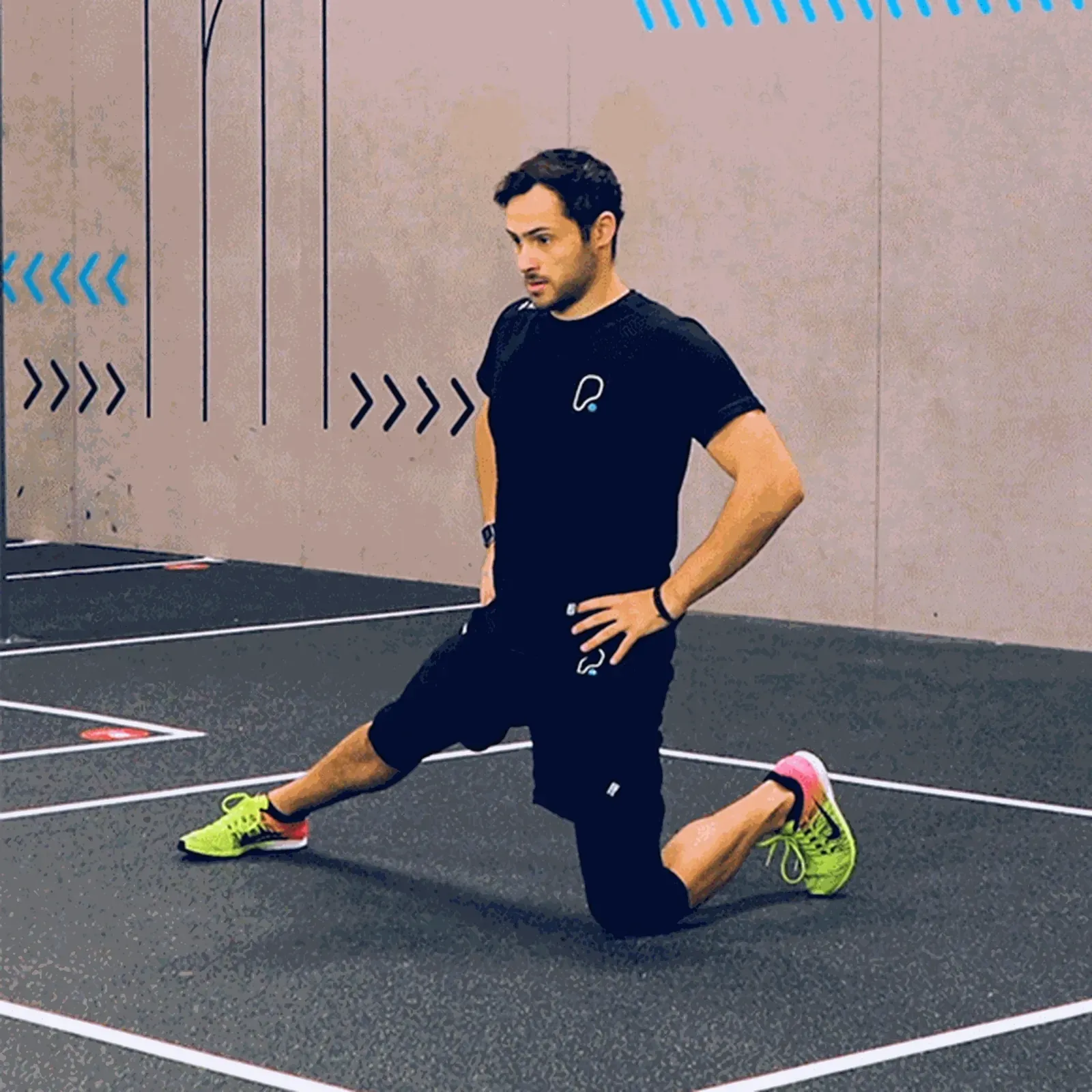 Man in black sportswear performing a kneeling lunge stretch on a gym floor
