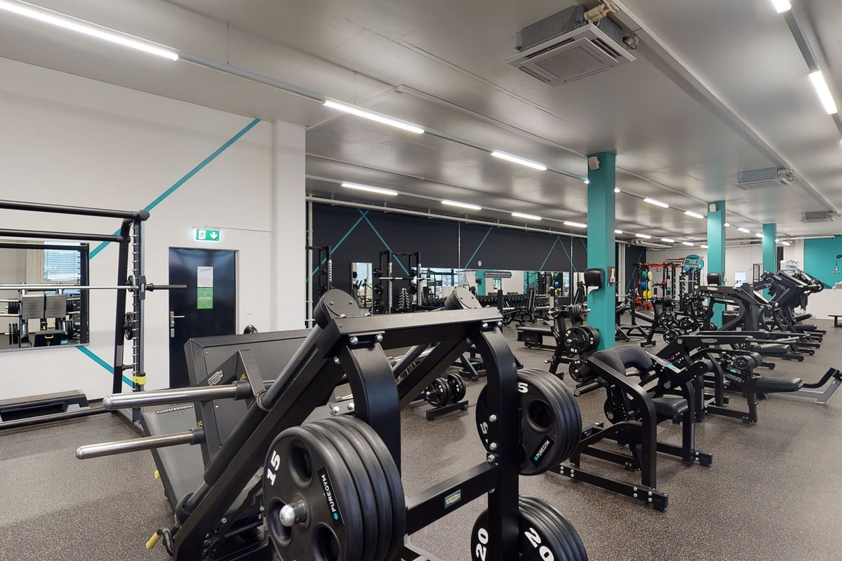 PureGym Kriens: Gym interior with weight machines, free weights, benches, squat racks, and rubberized flooring.