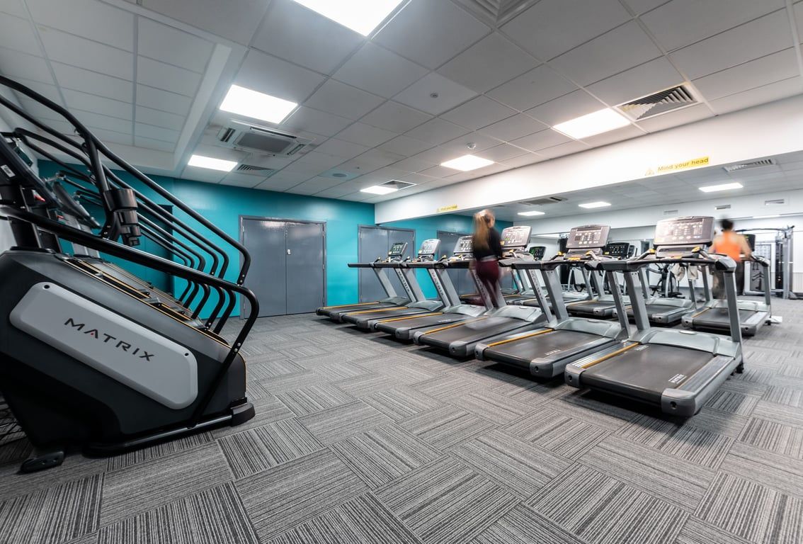 PureGym Bangor Northern Ireland: Rows of treadmills, turquoise accent walls, mirrored interior in a gym setting.