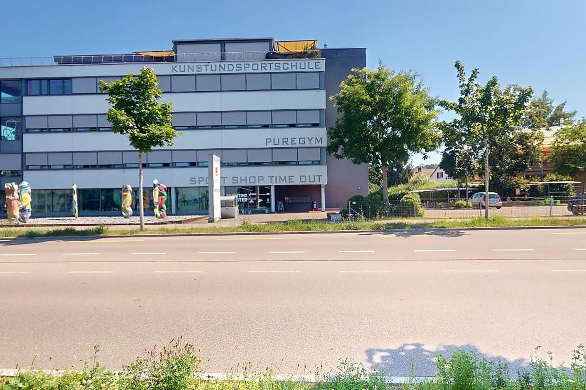 PureGym Uster: Extérieur du bâtiment avec signalisation du centre de conditionnement physique, arbres et stationnement visibles.