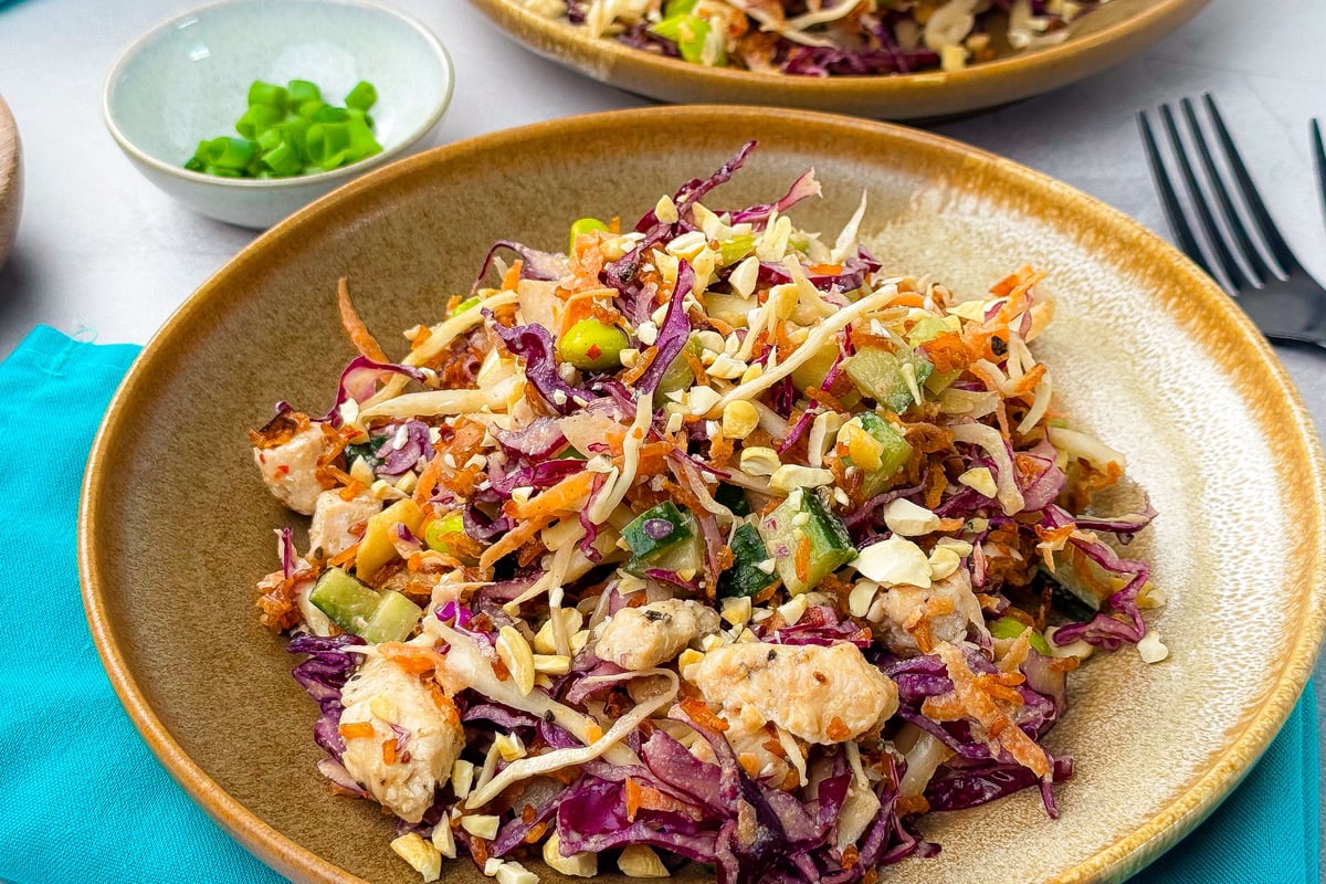 Colourful salad with shredded cabbage, carrots, chicken and nuts on a ceramic plate