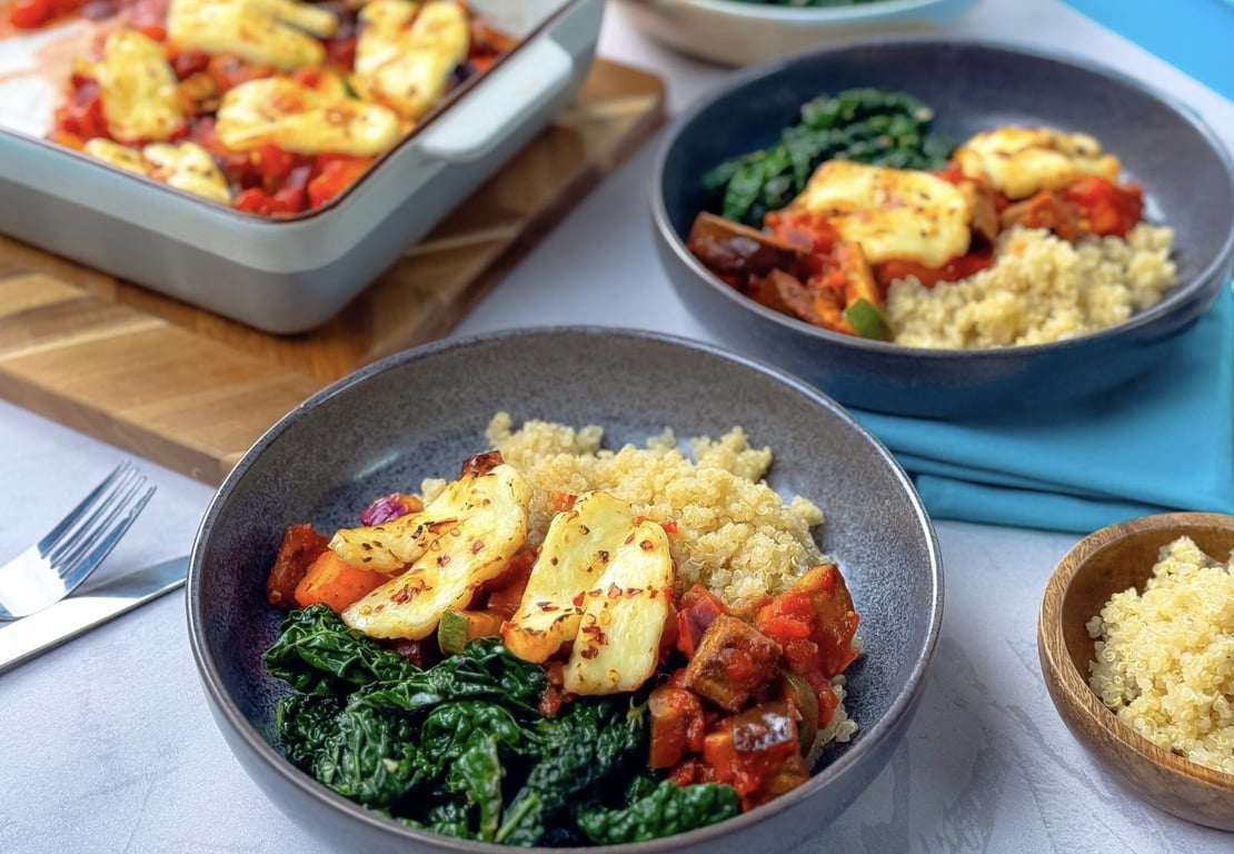 Two bowls with quinoa, cooked kale, roasted vegetables, and grilled halloumi cheese.
