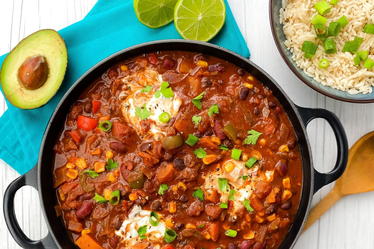 Black pot of chilli with beans, peppers and soured cream, served with rice and avocado