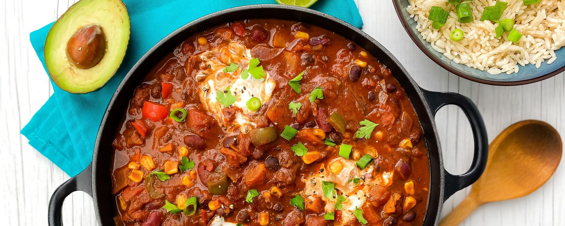 Black pot of chilli with beans, peppers and soured cream, served with rice and avocado