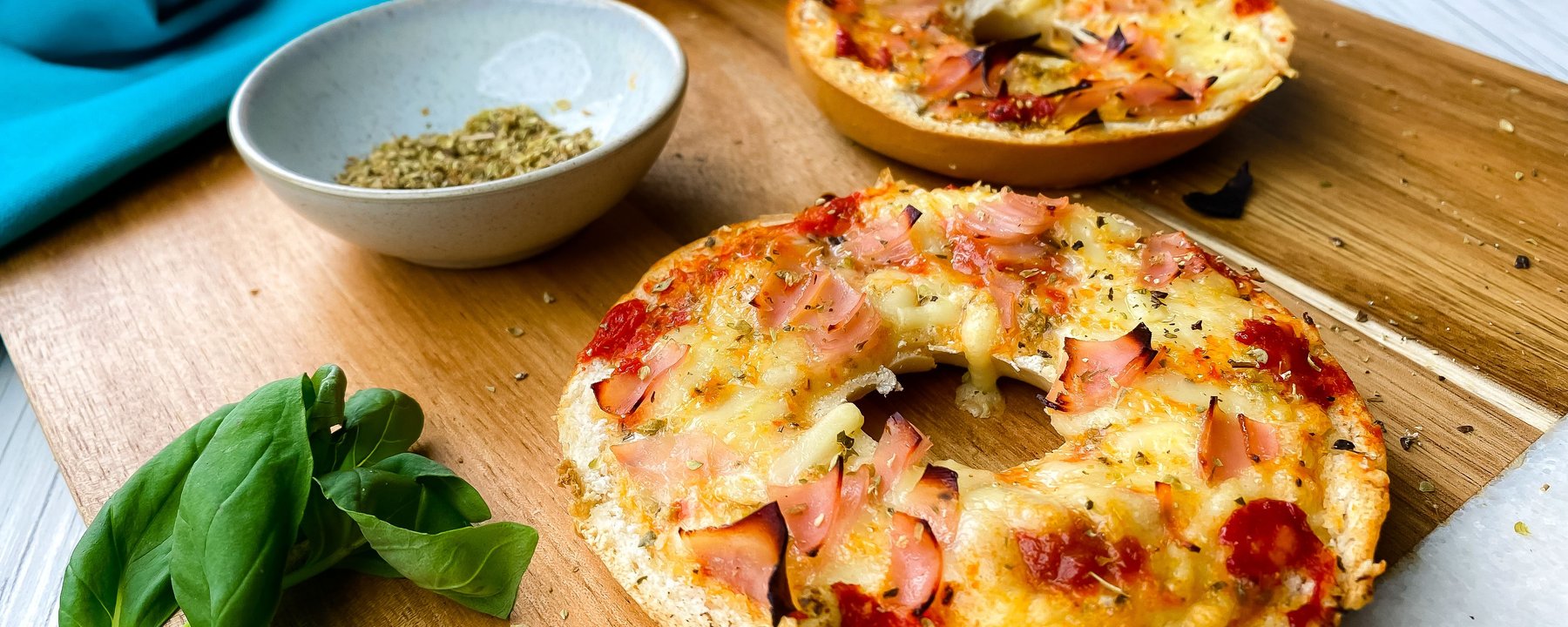 Two toasted bagel halves topped with melted cheese and ham on a wooden board