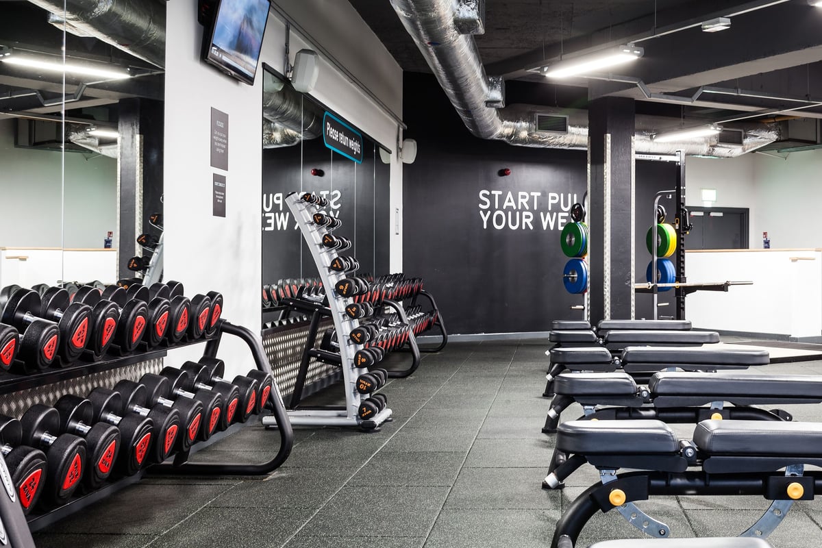 PureGym Manchester Stretford: Rows of weighted sleds, treadmills, free weights, and branded motivational wall graphics.