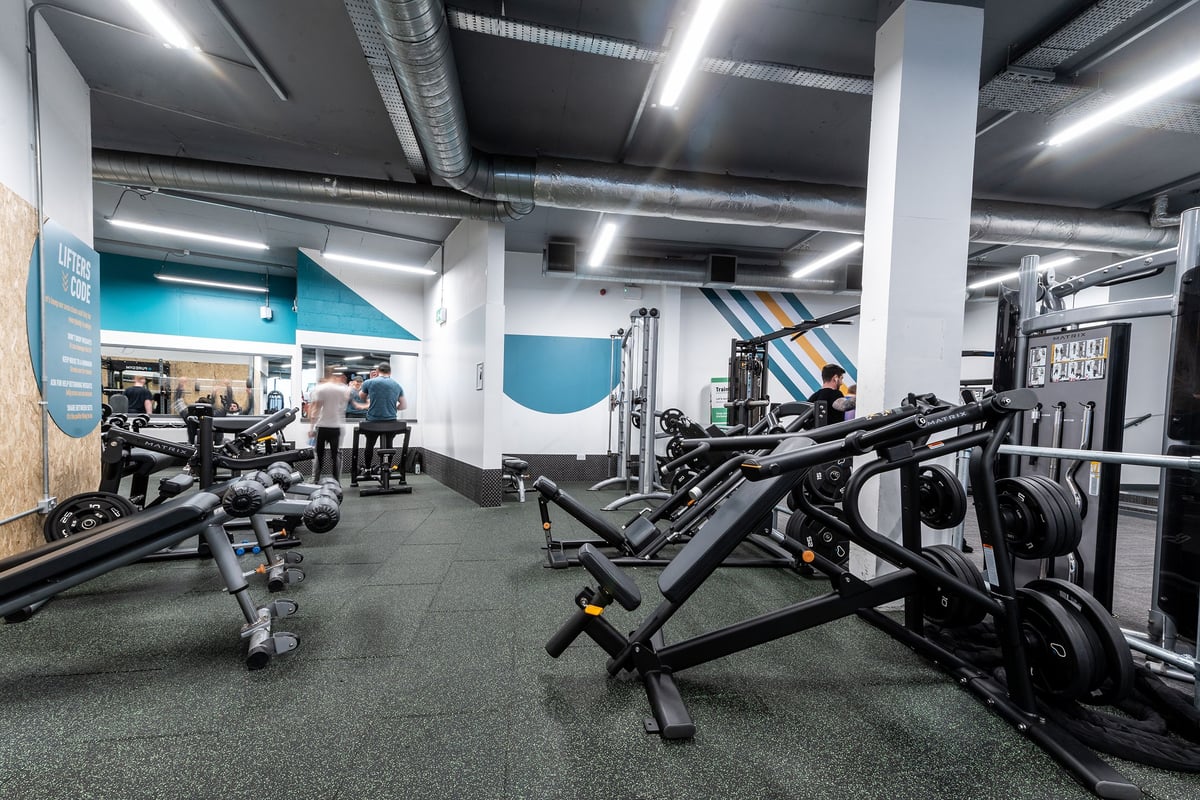 PureGym Walton-on-thames: Weightlifting area with benches, free weights, weight machines, and rubberized flooring.