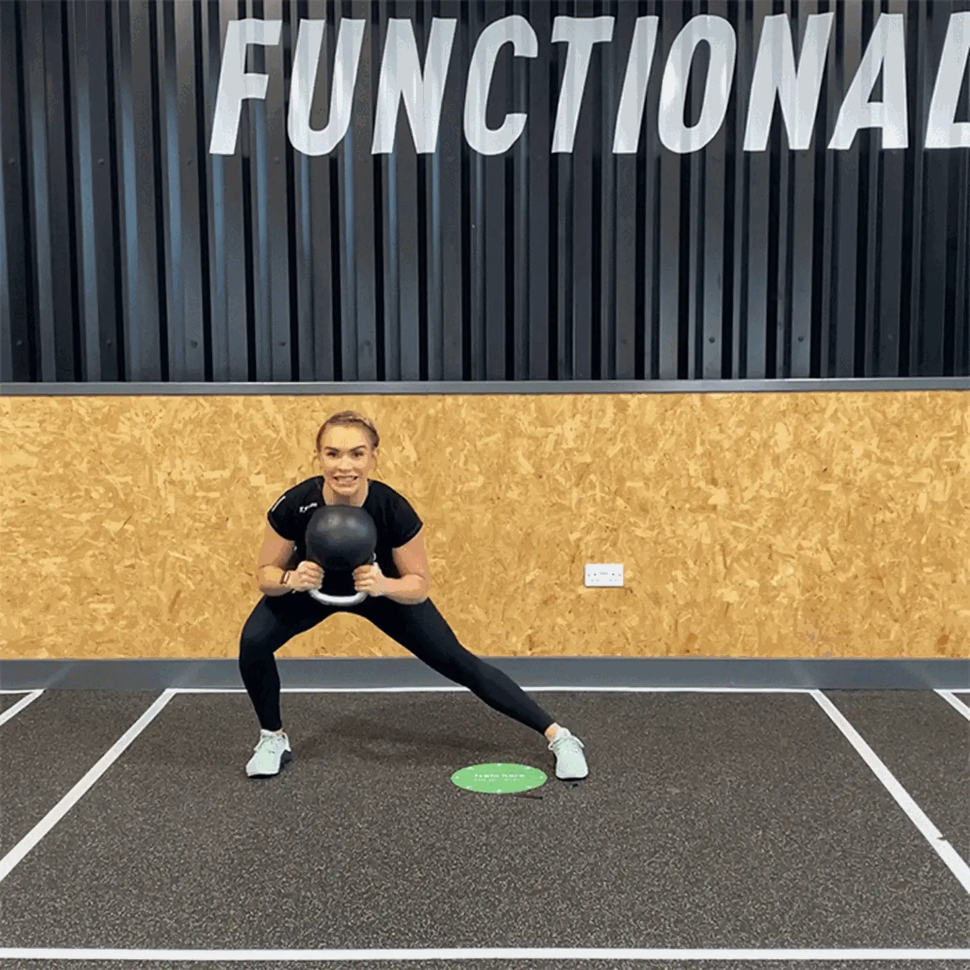 Woman in black sportswear holding kettlebell in a side lunge on gym floor