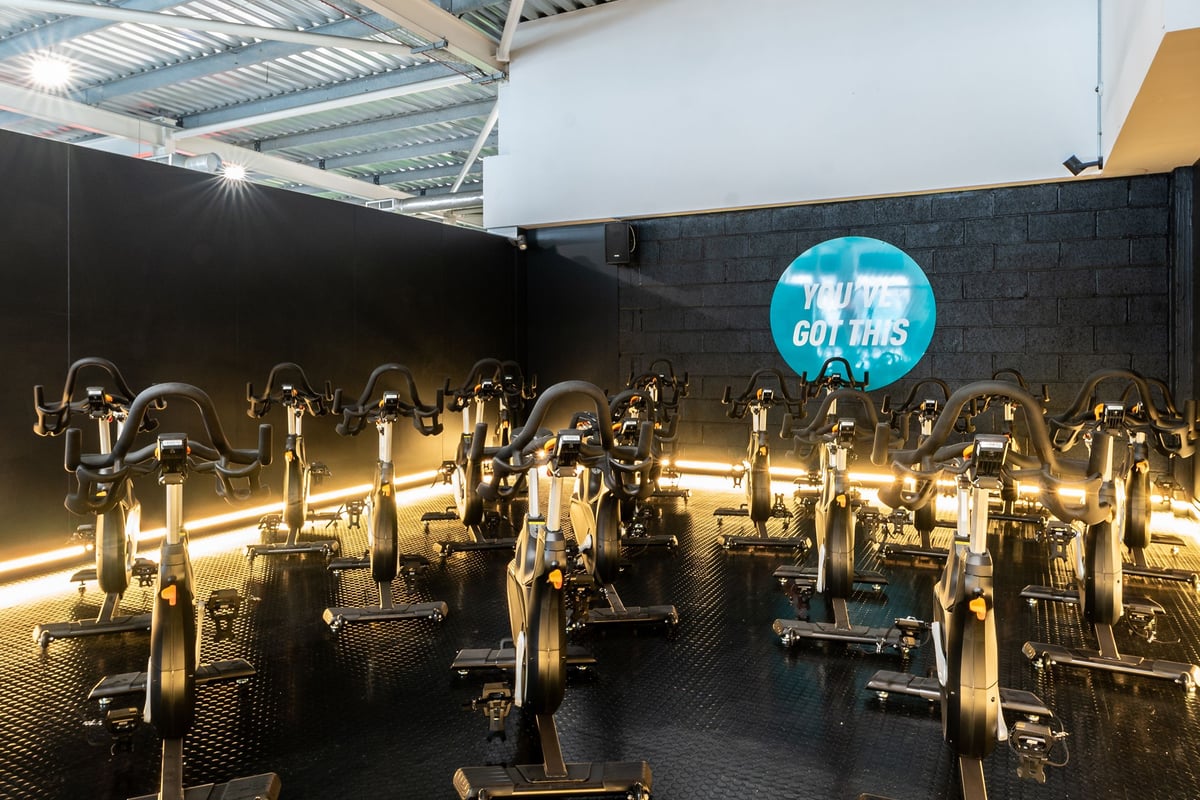 PureGym Bristol Union Gate: Rows of stationary exercise bikes with neon signage in a fitness studio.