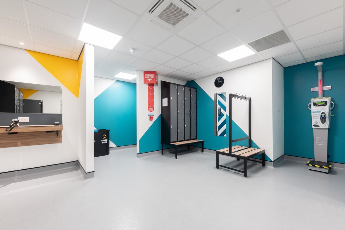 PureGym Southport: Locker room with benches, lockers, a reception desk, and accent colour walls.