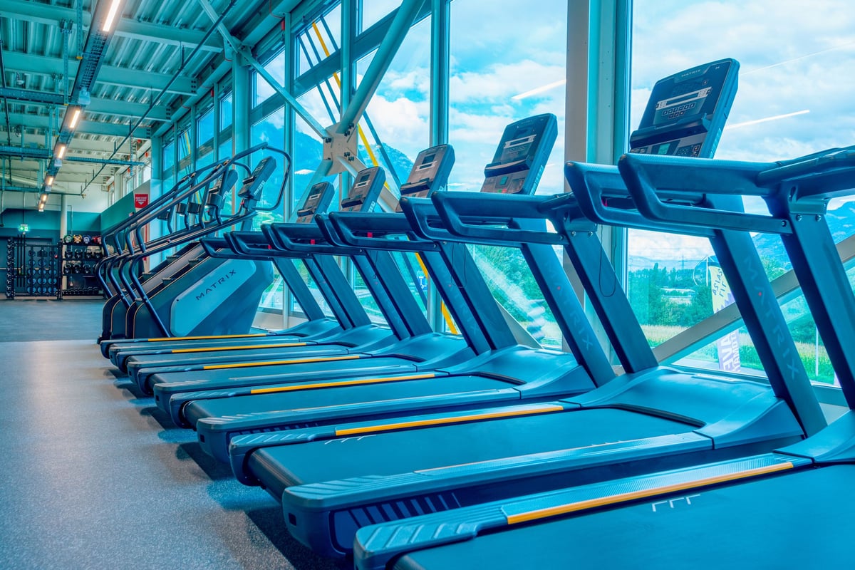 PureGym Martigny: Reihen von Laufbändern in einem luftigen, verglasten Fitnessbereich mit modernen Designmerkmalen.