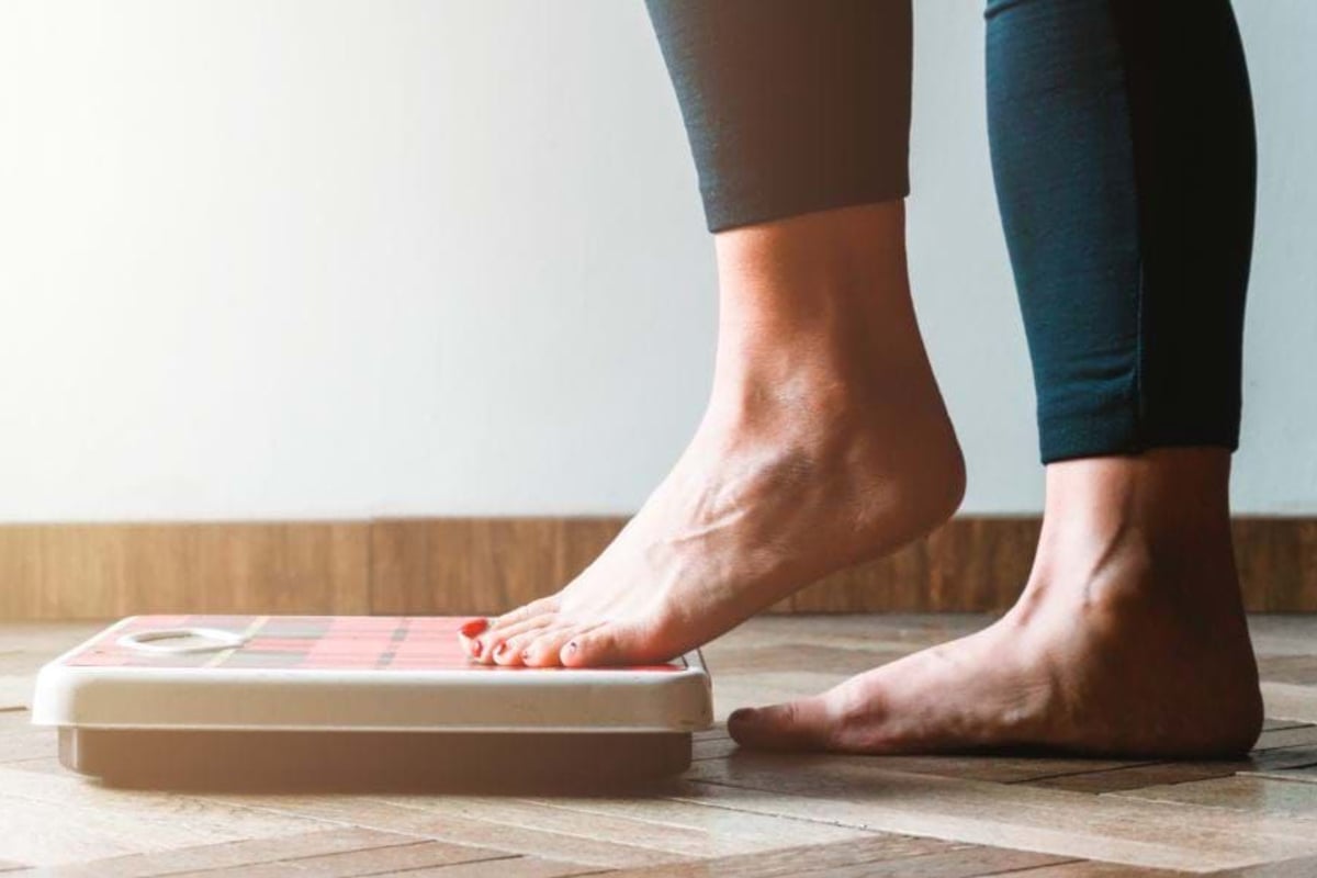 Bare feet stepping onto a weighing scale on a wooden floor against a white wall