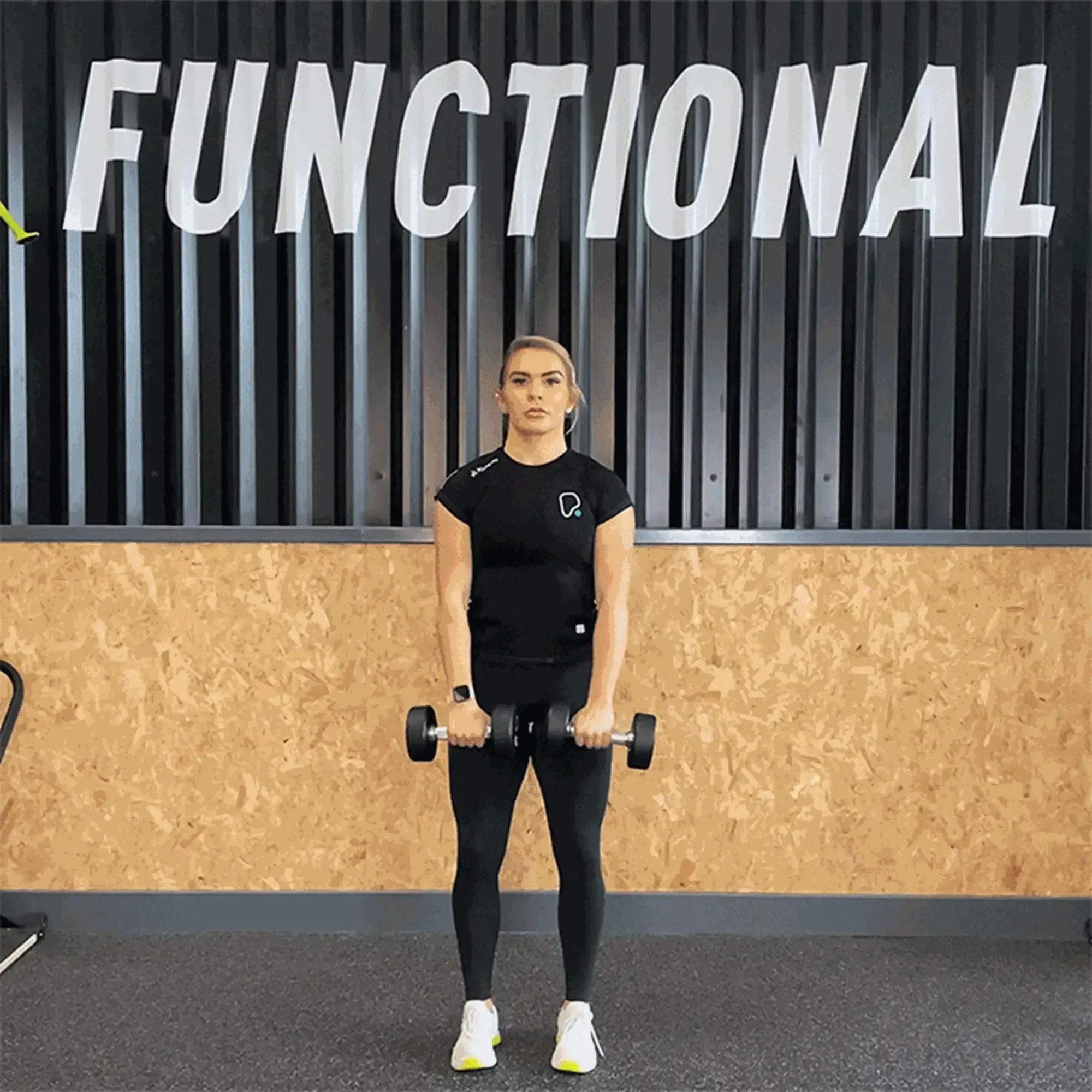Woman in black workout clothes lifting dumbbells in front of a wall with FUNCTIONAL text