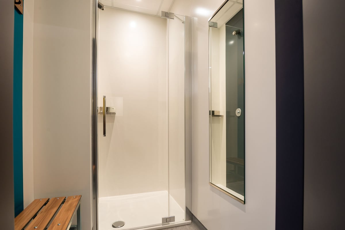 PureGym Wil: Cabine de douche privée avec porte vitrée, miroir et banc en bois.