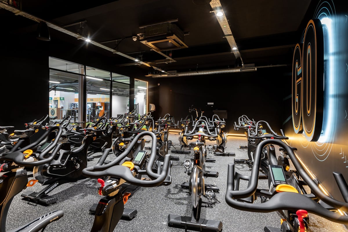 PureGym Bath Victoria Park: Rows of stationary exercise bikes with neon lighting in a dark gym interior.