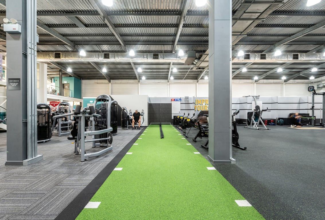 PureGym Milton Keynes Winterhill: Gym with turf runway, weightlifting platforms, machines, and rubberized flooring.