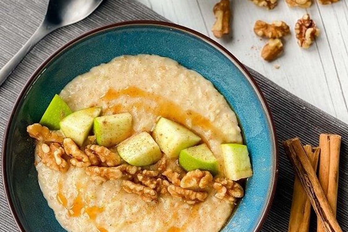 Porridge topped with walnuts, apple pieces, and honey drizzle in a blue bowl.