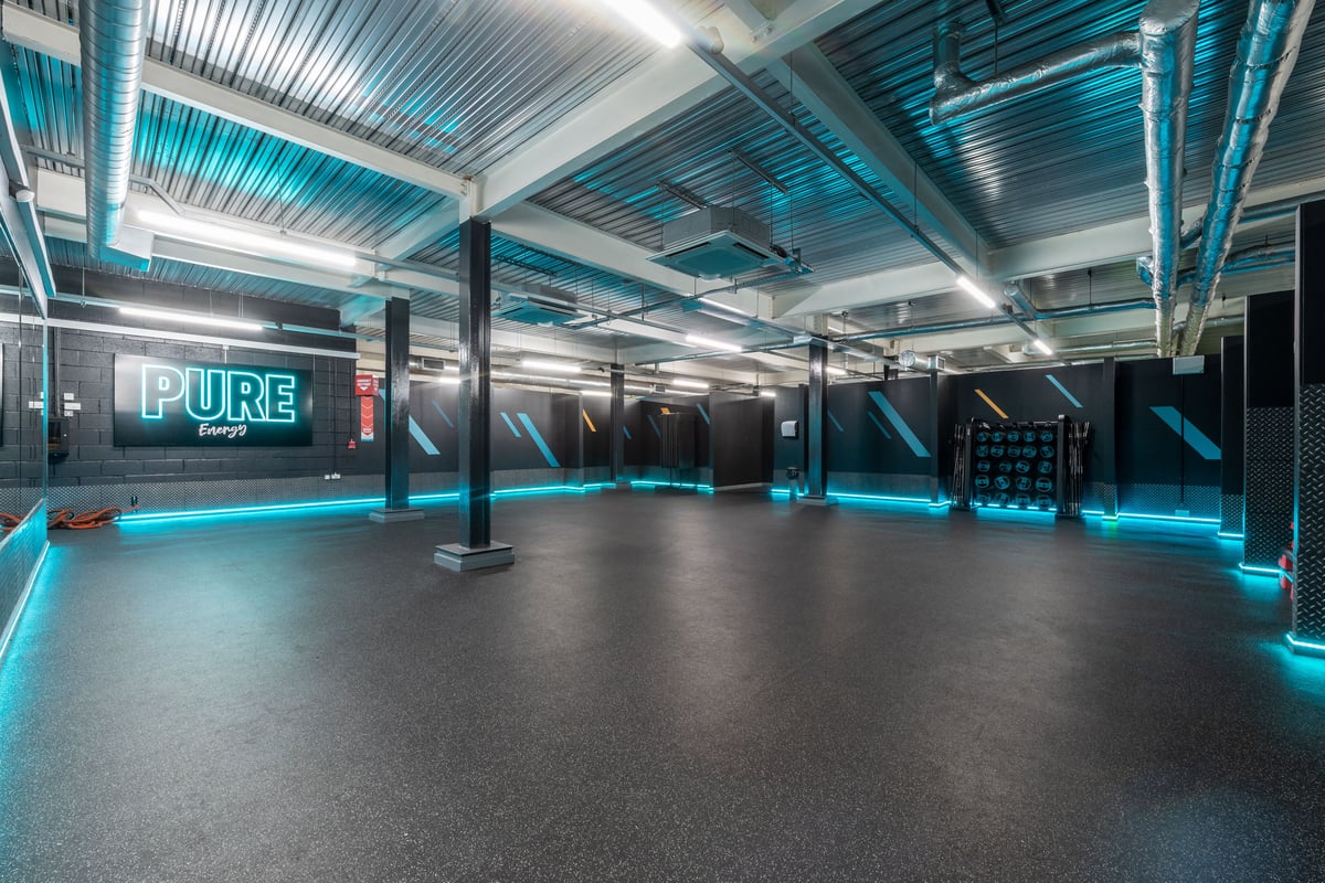PureGym Harrogate: Mirrored studio with suspended weights, neon lighting, and rubberized flooring.