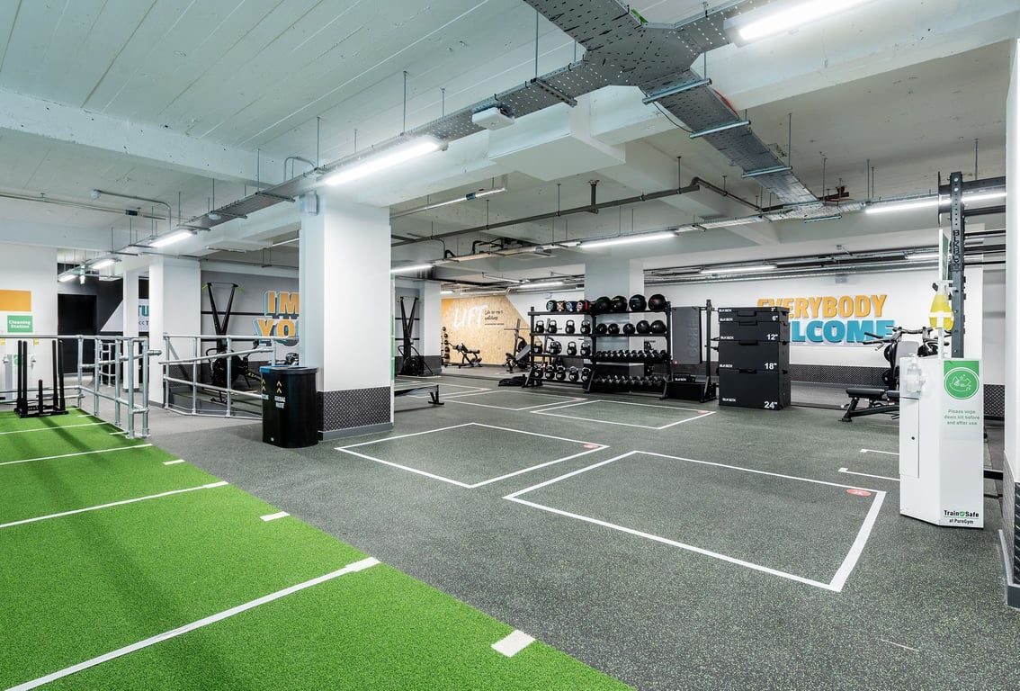PureGym London Holloway Road: Gym studio with turf area, weight racks, benches, resistance machines, and mirrored walls.