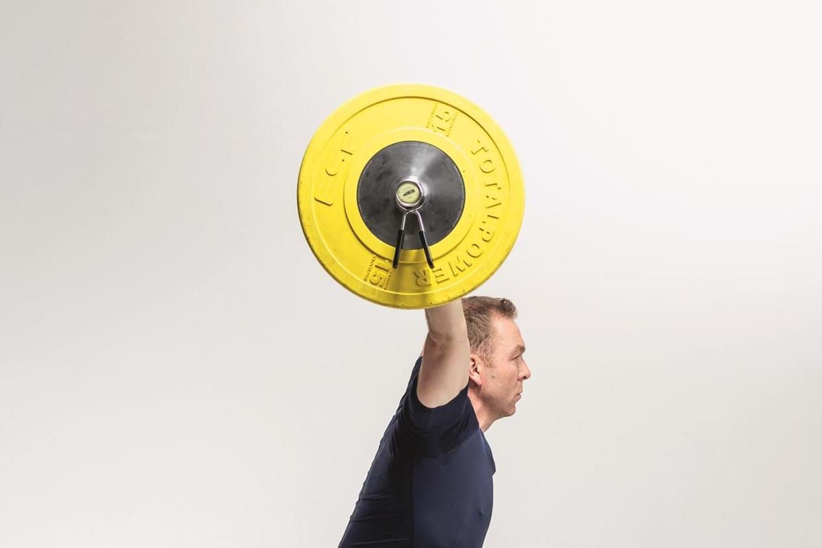 Man in navy sportswear squatting while holding a barbell with yellow weights overhead