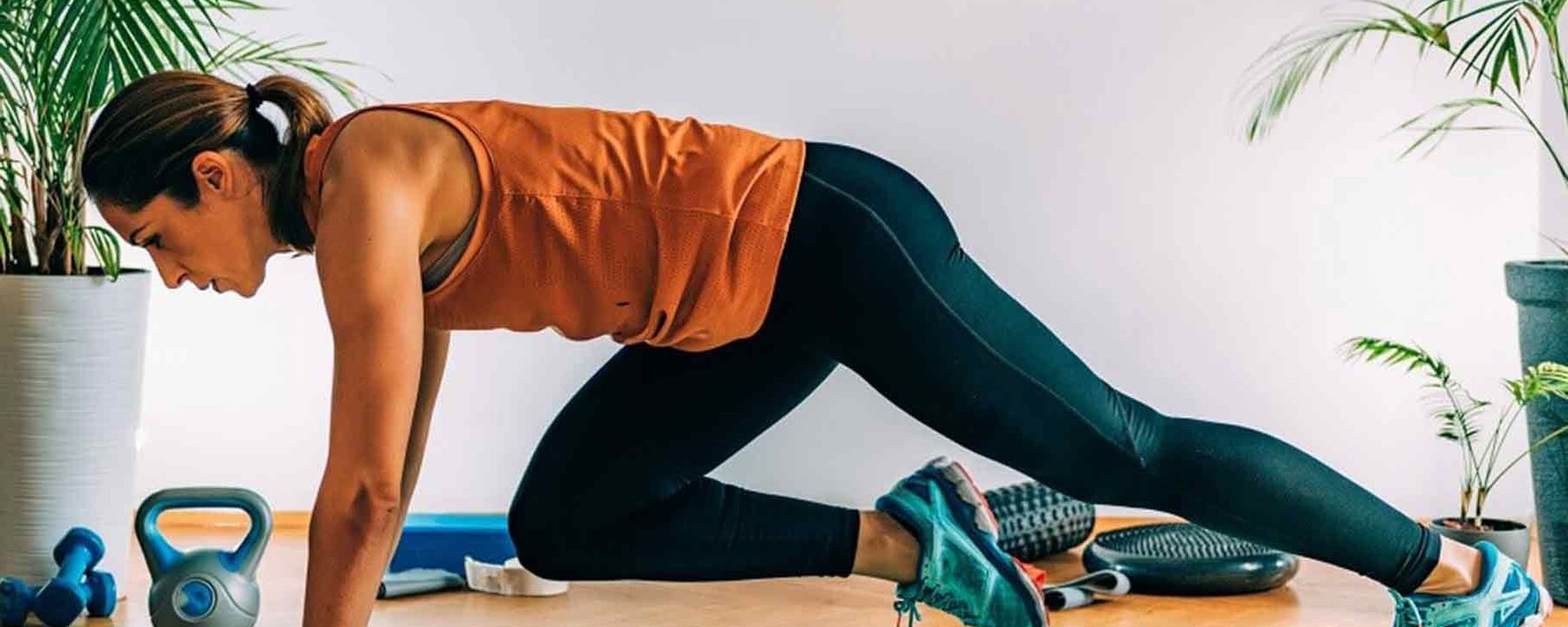 Donna con top arancione e leggings neri che fa esercizio mountain climber su tappetino