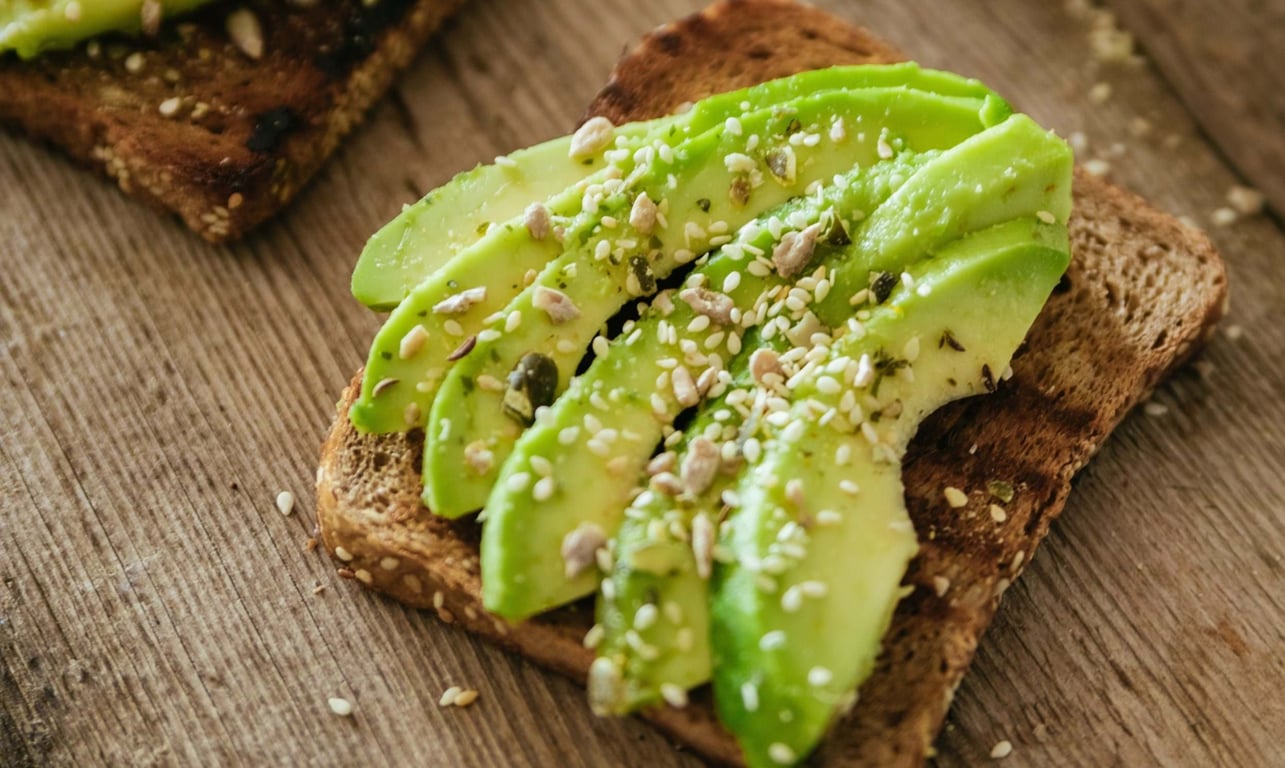 Sliced avocado with seeds on toasted whole grain bread on wooden surface