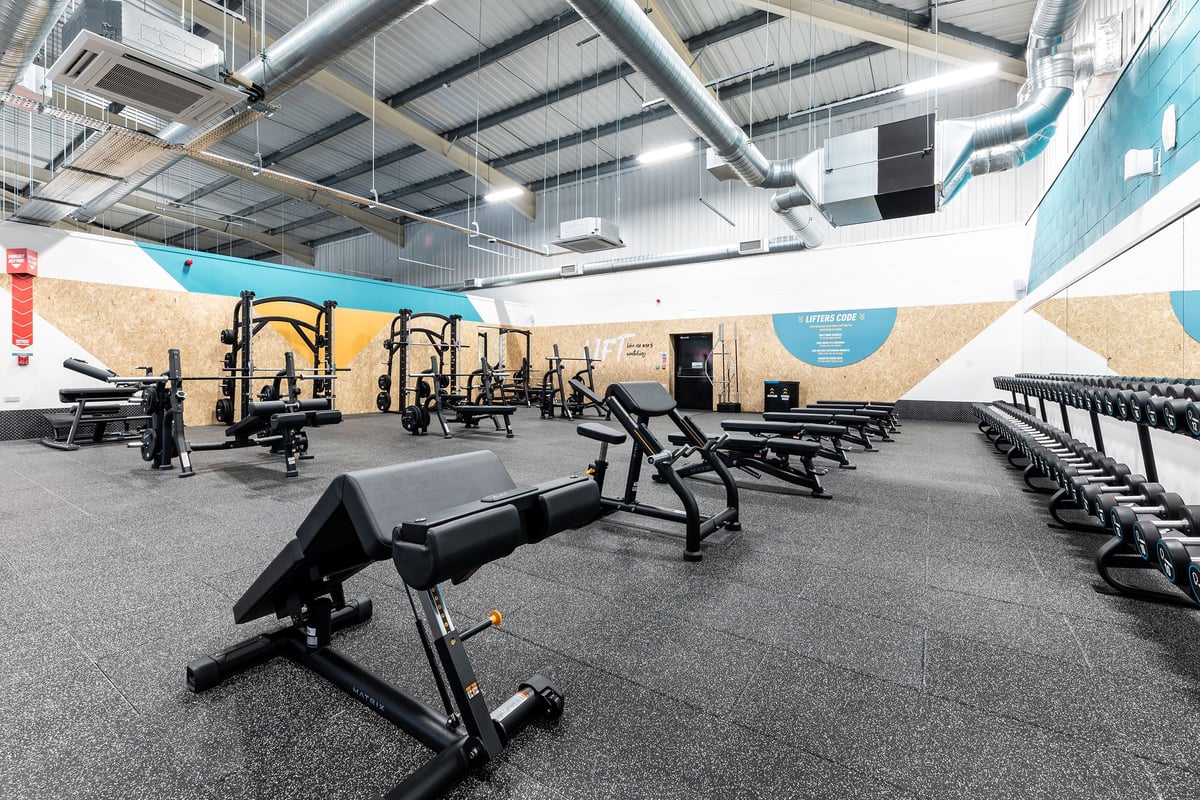 PureGym Merthyr Tydfil: Rows of weight benches, squat racks, free weights and lifting equipment on rubberized flooring.