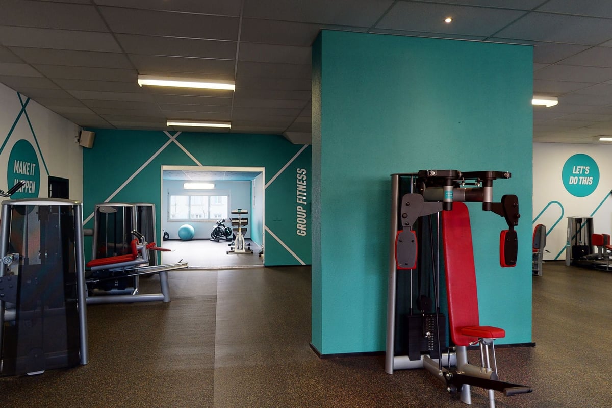 PureGym Rorschach: Entrée du gymnase avec sacs de boxe rouges, appareils de musculation, murs bleu sarcelle et sol caoutchouté visibles.
