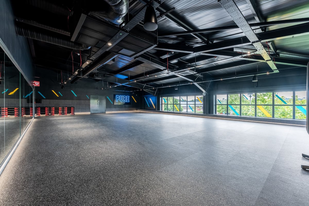 PureGym Sheffield Crystal Peaks: Interior gym space with rubberized flooring, exposed ceiling ducts, and floor markings.