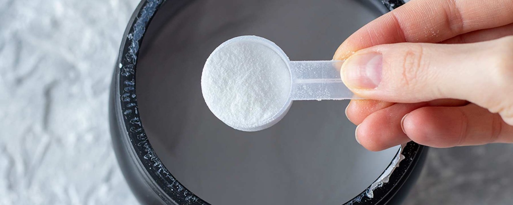 Main tenant une cuillère de poudre blanche au-dessus d’un récipient noir ouvert sur surfac