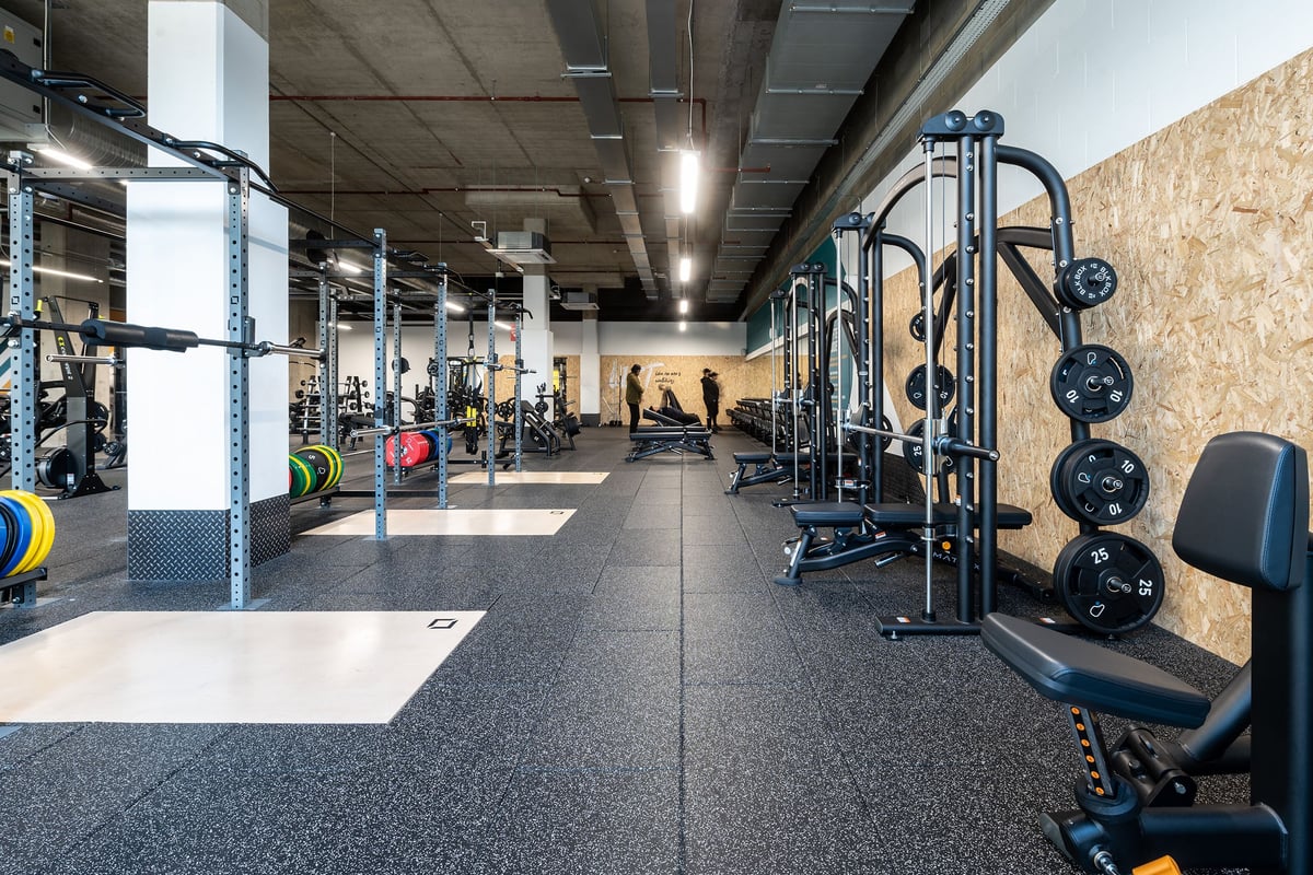 PureGym London Woolwich: Strength training area with squat racks, weight plates, benches, and rubberized flooring.
