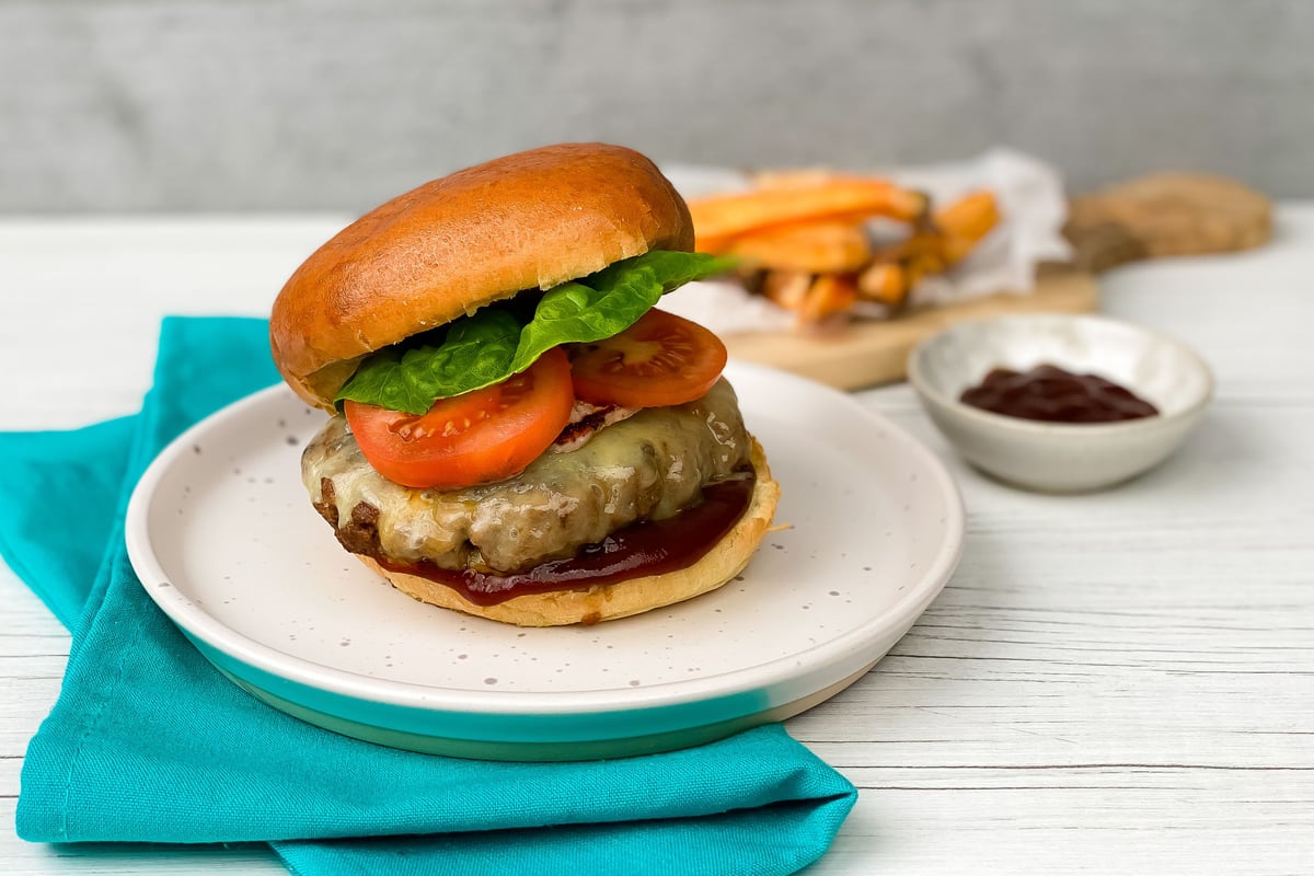Cheeseburger with melted cheese, tomato and lettuce on a white plate with turquoise napkin