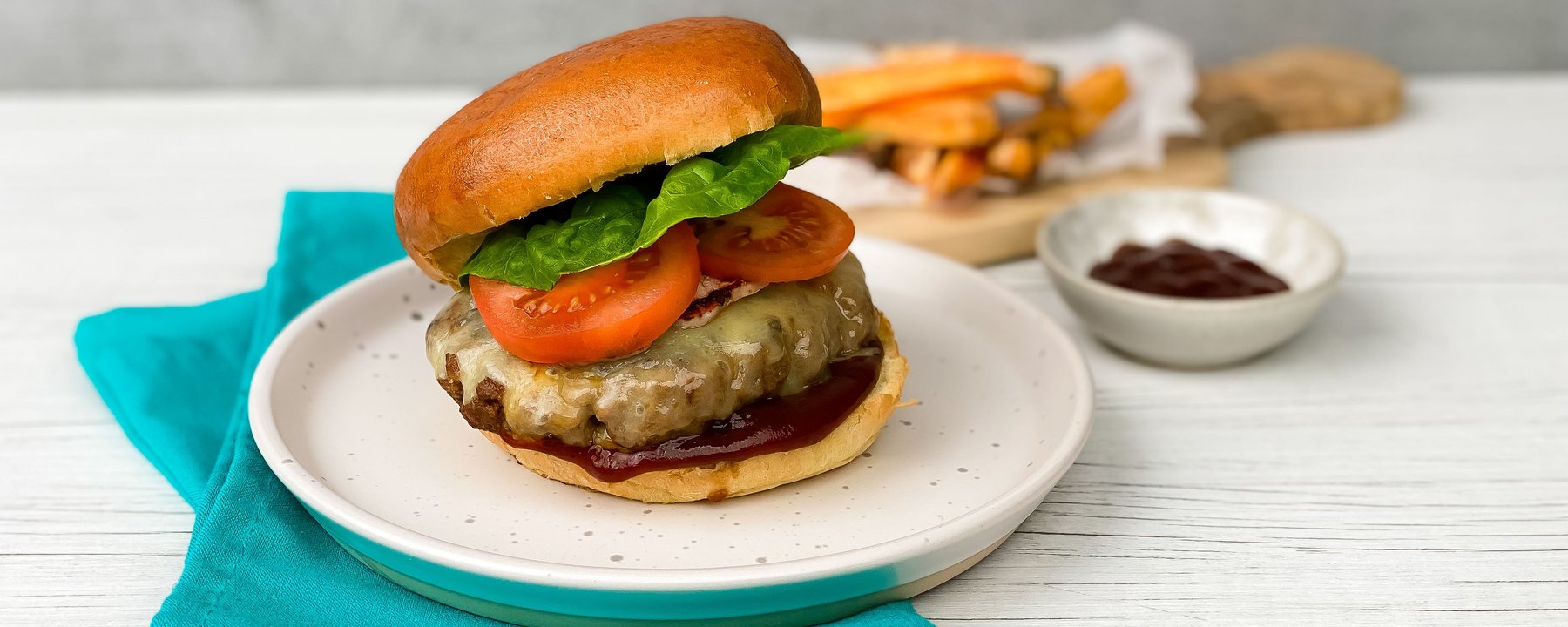 Cheeseburger with melted cheese, tomato and lettuce on a white plate with turquoise napkin