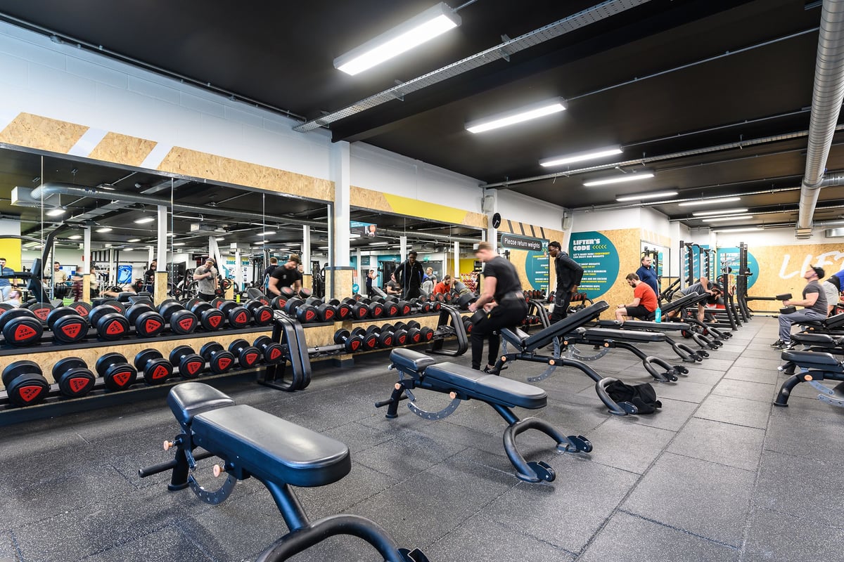 PureGym Oxford Templars Shopping Park: Weights, benches, rubberized flooring in a dimly lit, industrial-style gym interior.
